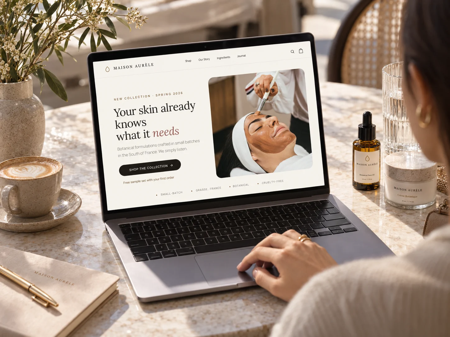 Maison Aurèle's homepage on a laptop, with a woman typing at a café table