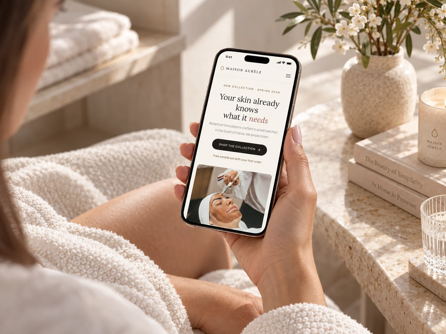 Maison Aurèle's homepage on a phone held by a woman in a robe